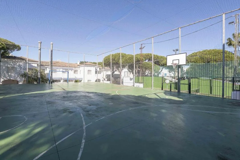 An outdoor sports court with a basketball hoop and fenced perimeter.