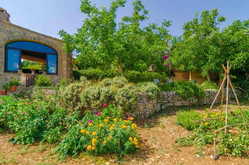 A garden with flowering plants and trees beside a stone building.