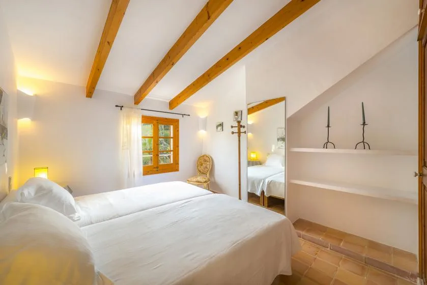 A bedroom with a bed, exposed ceiling beams, and a window.