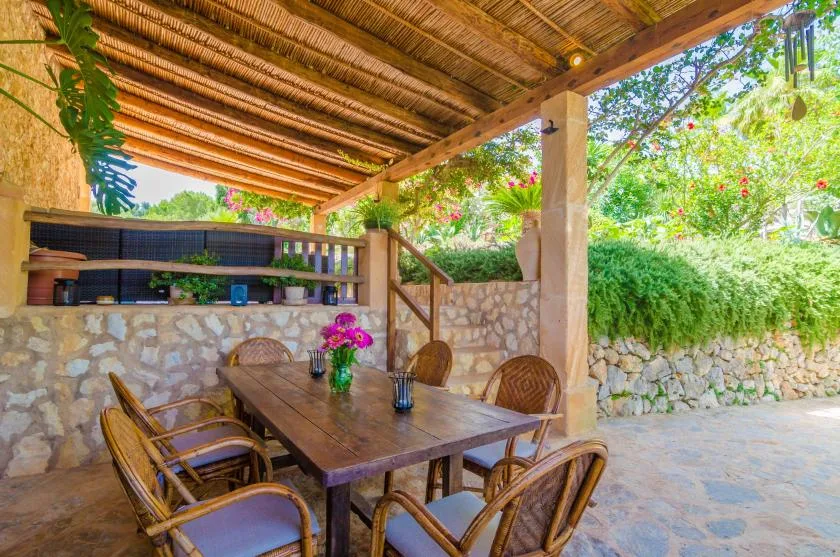 A covered outdoor dining area with a wooden table and surrounding greenery.