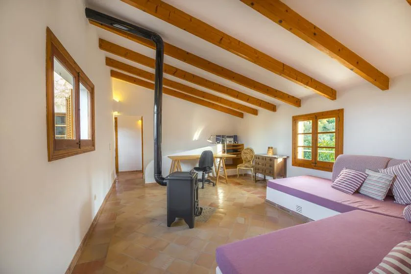 A bright attic living area with exposed wooden beams, seating, and a desk.