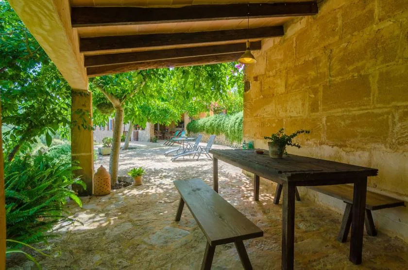 A shaded outdoor dining area with a wooden table beneath a covered stone patio.