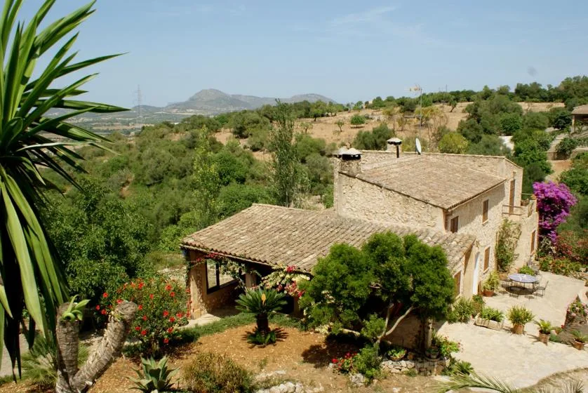 A stone house sits among gardens on a green hillside.