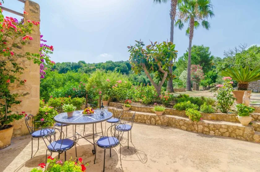 A garden patio with an outdoor table and chairs among flowering plants.