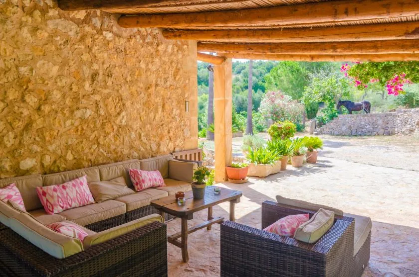 A covered outdoor seating area with cushioned wicker furniture opens onto a garden.