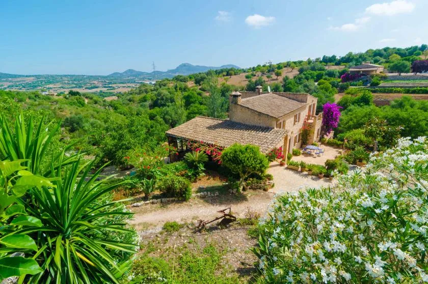 A countryside house sits among lush gardens, with hills stretching across the background.