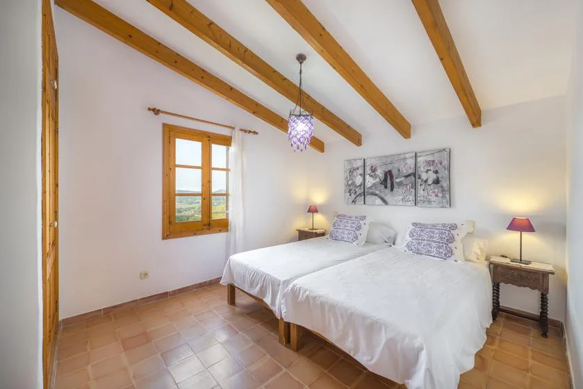 A bright bedroom with two beds, wooden ceiling beams, and a window.
