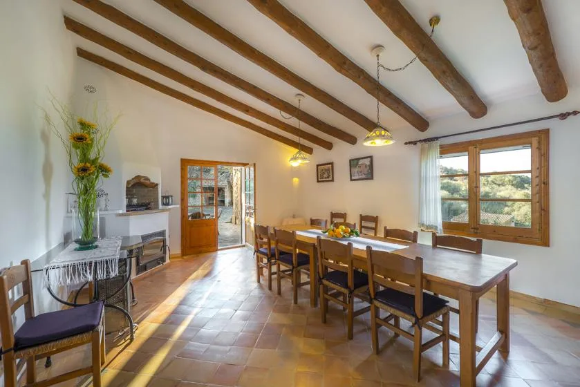 A dining room with a long wooden table beneath exposed ceiling beams.