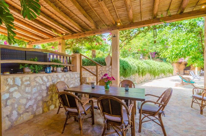 A covered outdoor dining area with a table and chairs beside a garden.