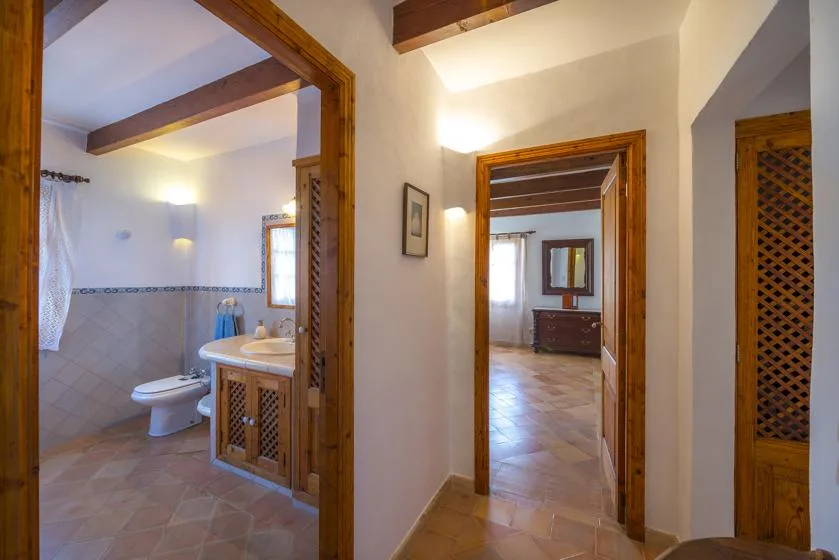 A hallway with wooden doorways opens onto a bathroom and an adjoining room.