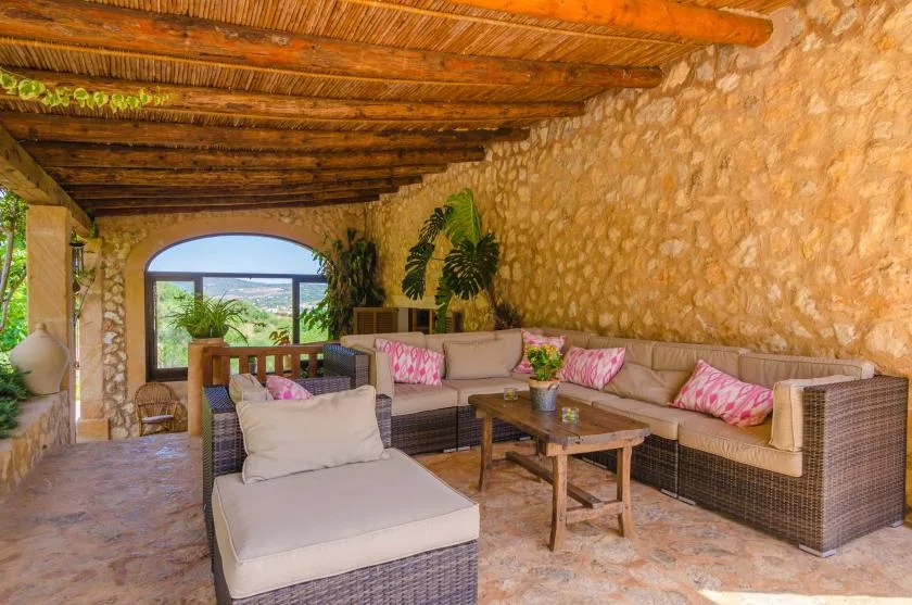 A covered outdoor seating area with cushioned wicker furniture and a wooden coffee table.