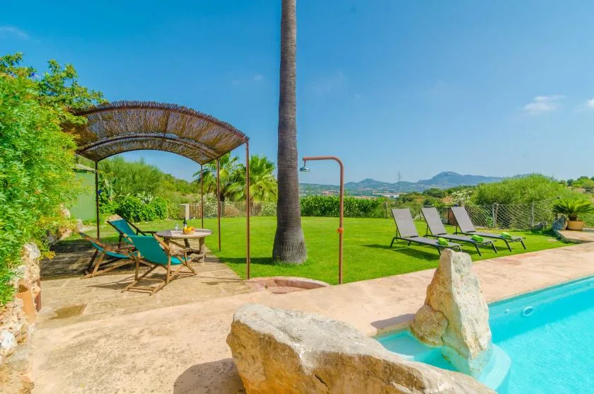 A sunny outdoor pool area with lounge seating and a shaded table.
