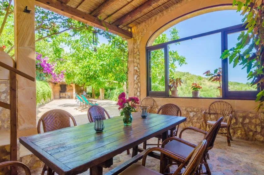 A covered outdoor dining area with a wooden table and garden views.