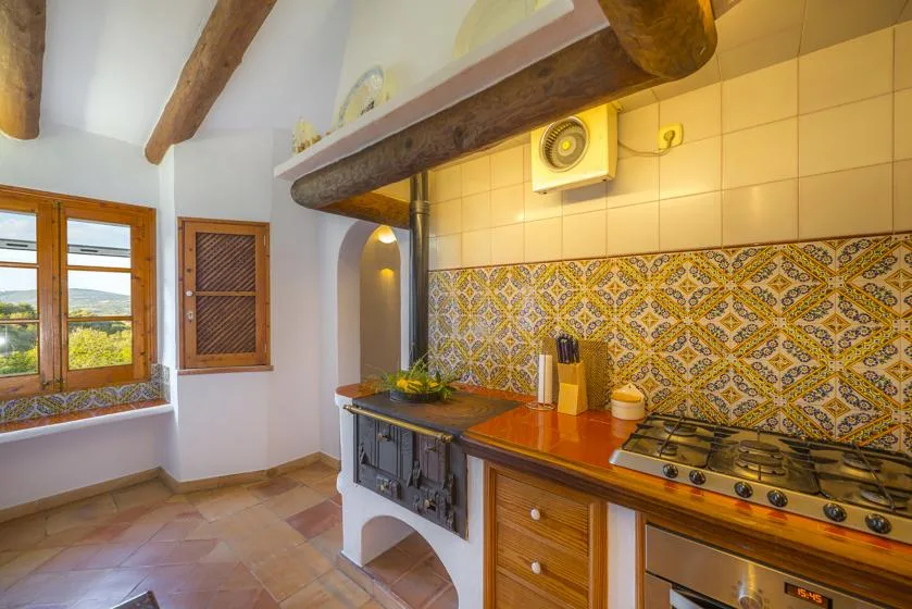 A rustic kitchen with a tiled backsplash, cooktop, and wooden ceiling beams.