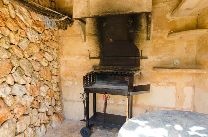 A barbecue grill stands in a rustic stone-walled cooking area.