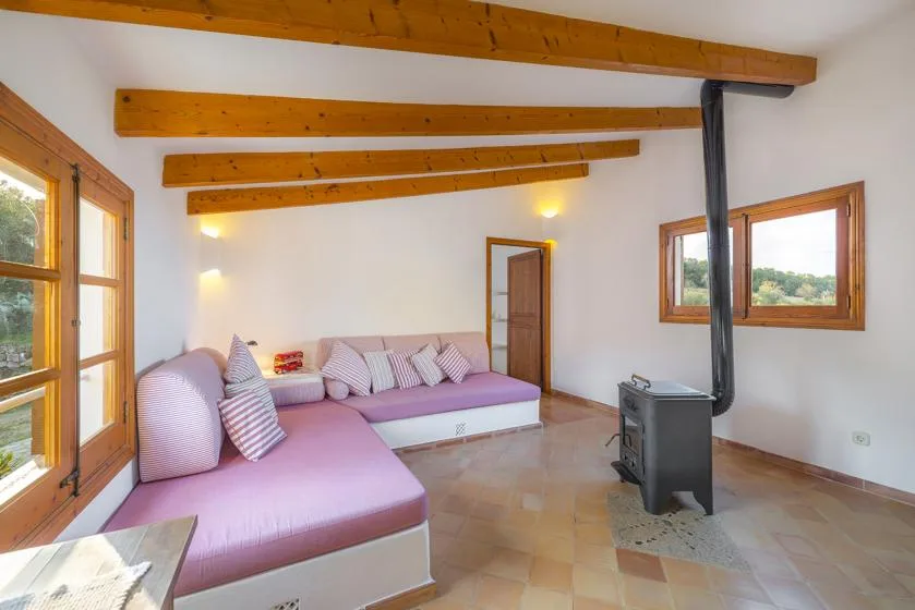 A bright living room with L-shaped seating, wooden ceiling beams, and large windows.