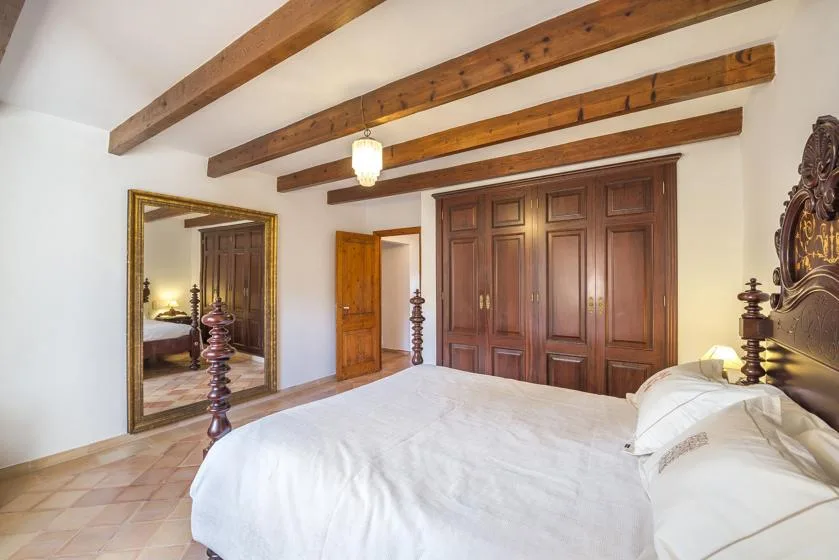 A bedroom with a large bed, wooden wardrobes, and exposed ceiling beams.