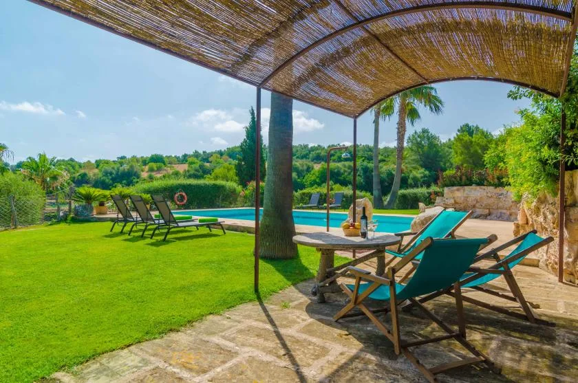A shaded outdoor seating area overlooks a swimming pool and green lawn.