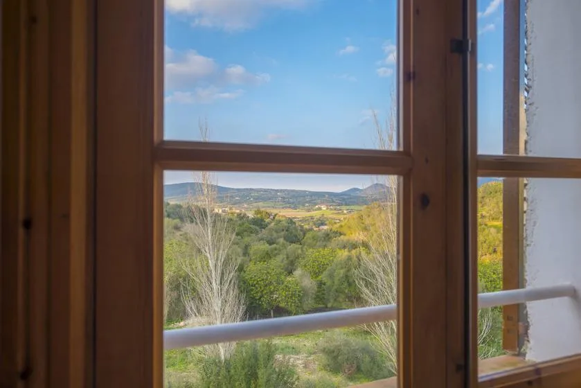 A view through wooden-framed windows overlooks green hills beneath a blue sky.