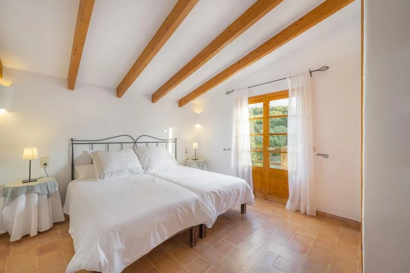 A bright bedroom with a bed beneath exposed wooden ceiling beams.