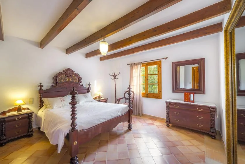 A bedroom with a large wooden bed, exposed ceiling beams, and a window.