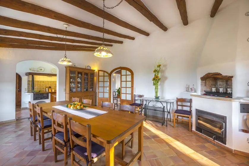 A dining room with a long wooden table beneath exposed ceiling beams.