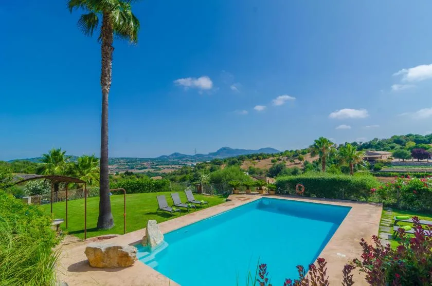 Outdoor swimming pool surrounded by greenery, with hills visible in the distance.
