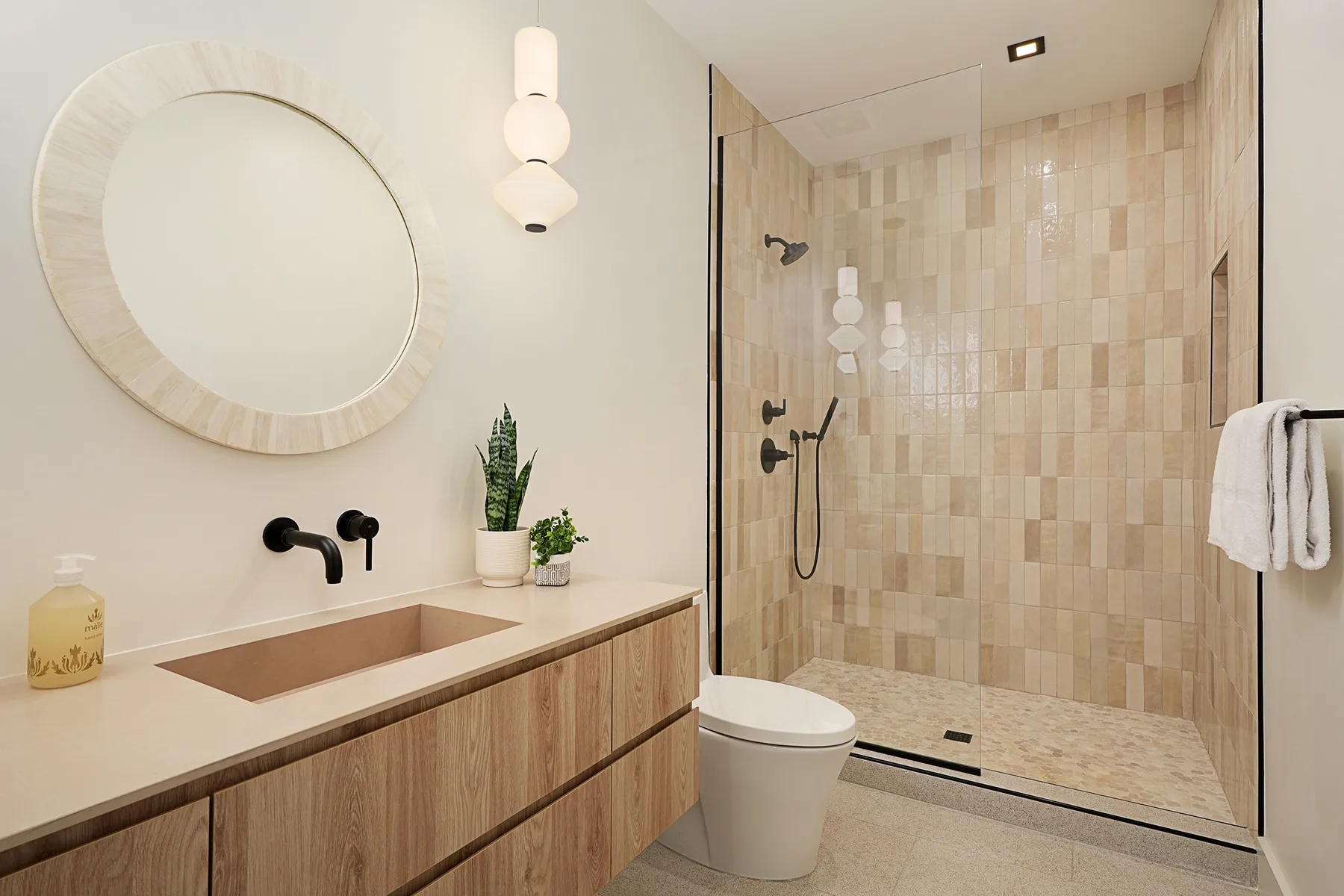 Un baño con un espejo redondo grande, lavabo y ducha con azulejos.
