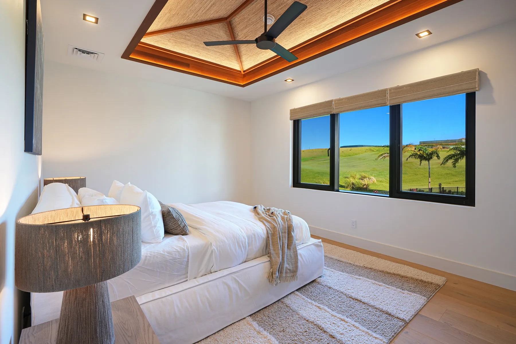 Un dormitorio con una cama junto a una ventana grande con vista a campos verdes.