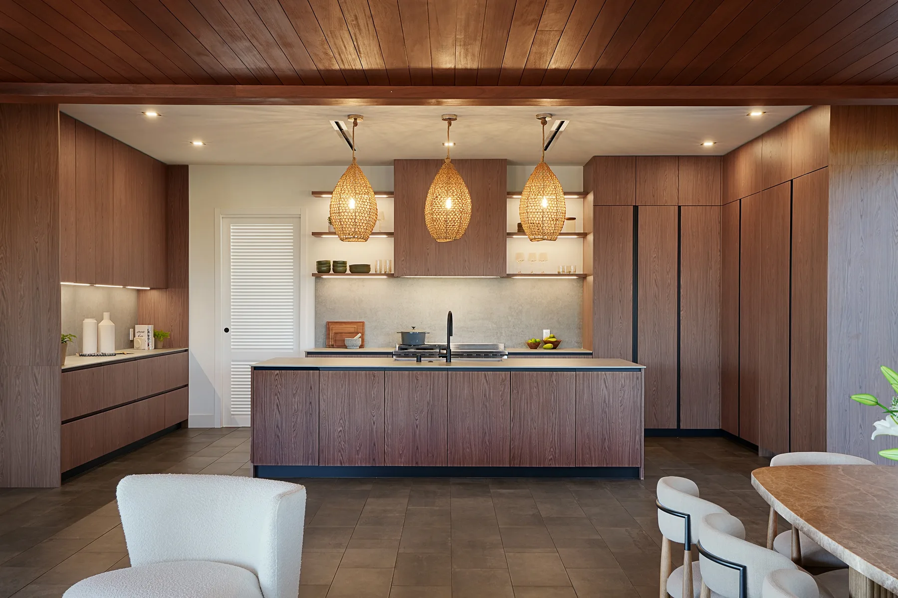 Una cocina moderna con una isla central, gabinetes de madera y lámparas colgantes tejidas.