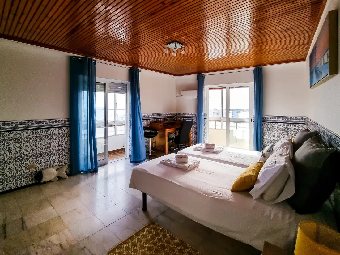 Dormitorio con una cama, cortinas azules y techo de madera.