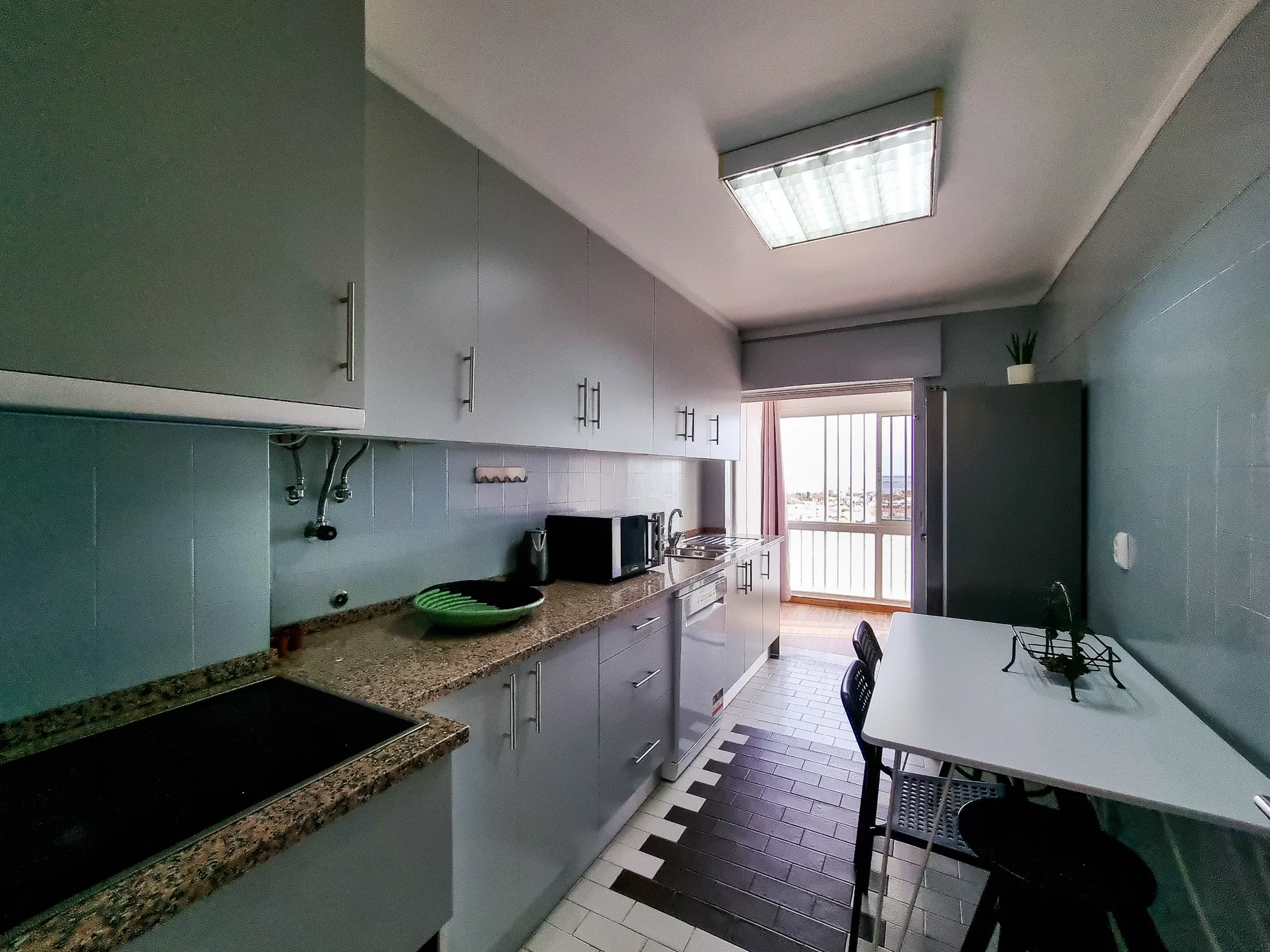 Una cocina estrecha con armarios y una mesa junto a una ventana luminosa.