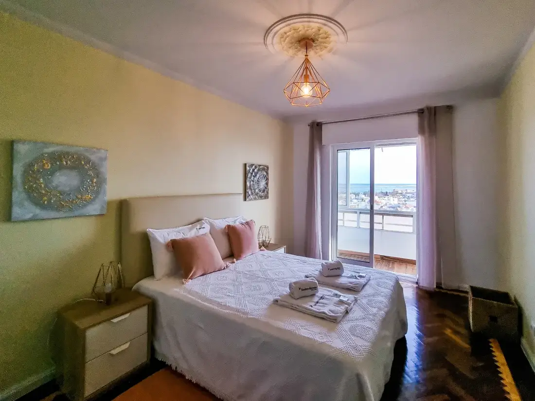 Un dormitorio con una cama, mesitas de noche y una puerta de cristal que da a un balcón.