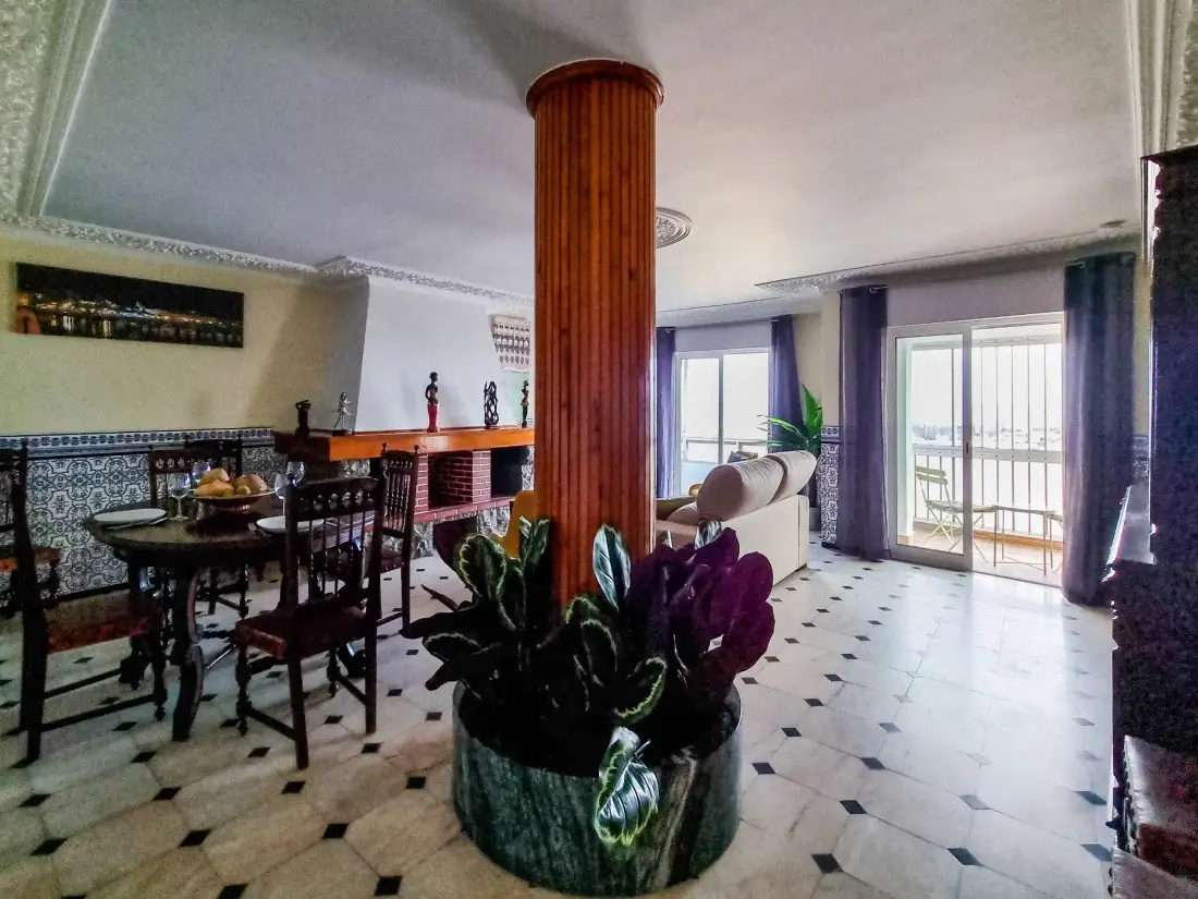 Comedor y sala de estar con una mesa, asientos y puertas de vidrio que dan a un balcón.