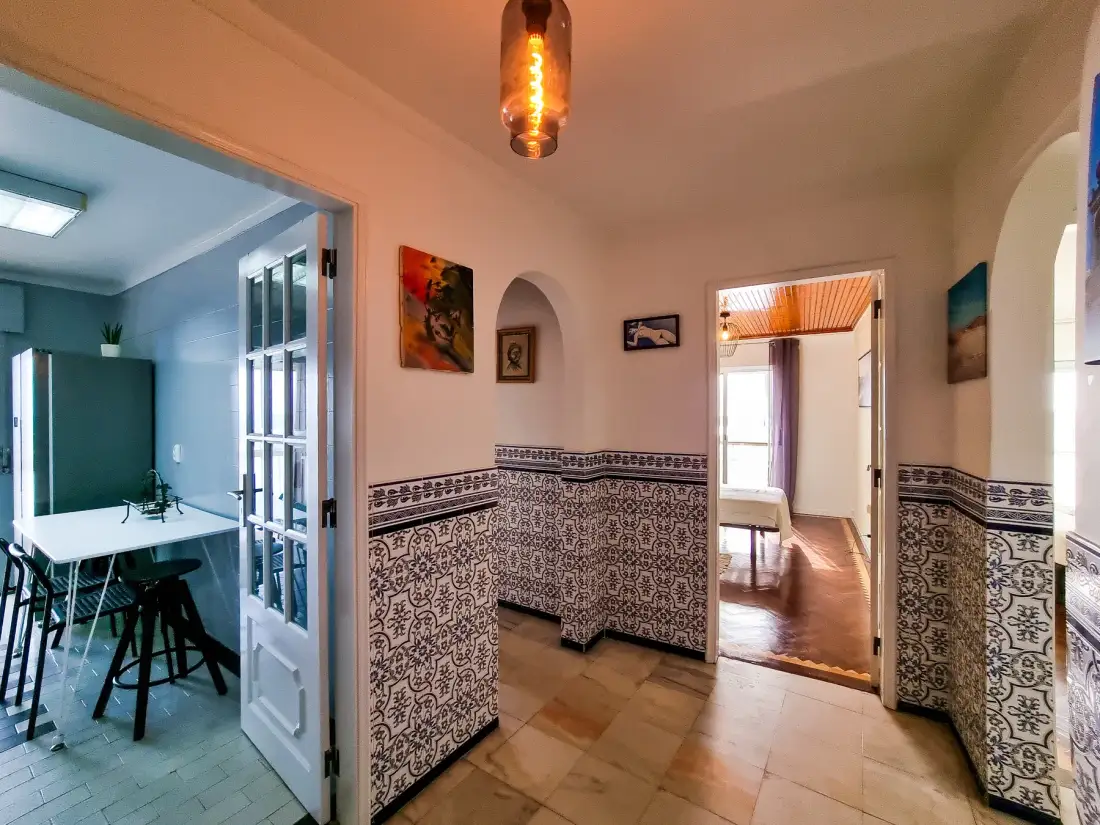 Un pasillo de apartamento con azulejos conecta con un comedor y una habitación luminosa.