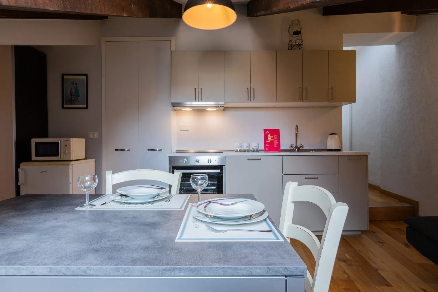 A dining table set for a meal faces a bright kitchen with pale cabinets.