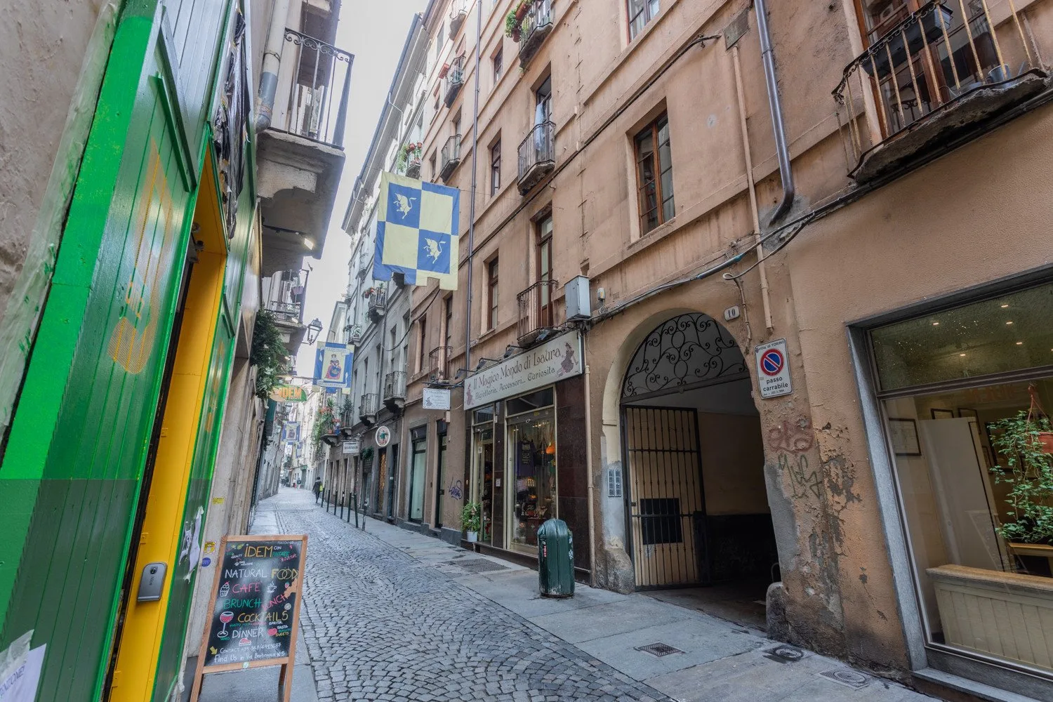 A narrow cobblestone street runs between closely spaced buildings and storefronts.