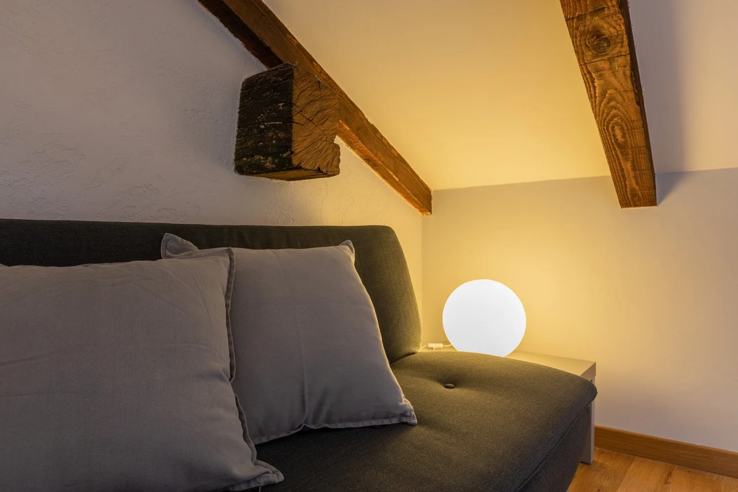 A bedroom seating area with gray cushions beneath exposed wooden beams.