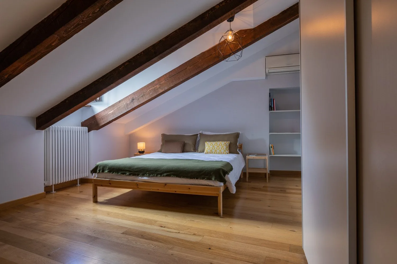 A bedroom with a bed beneath a sloped ceiling and exposed wooden beams.