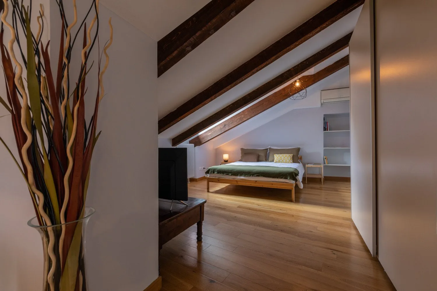 A bedroom with a bed beneath sloping ceilings and exposed wooden beams.