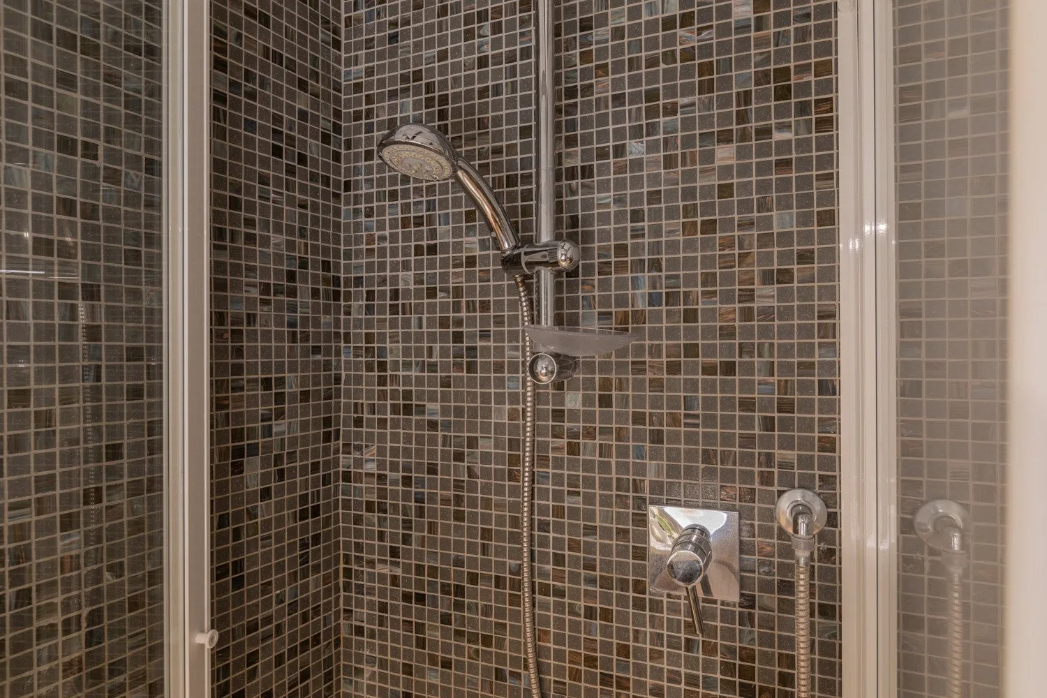 A tiled shower with a handheld showerhead and wall controls.