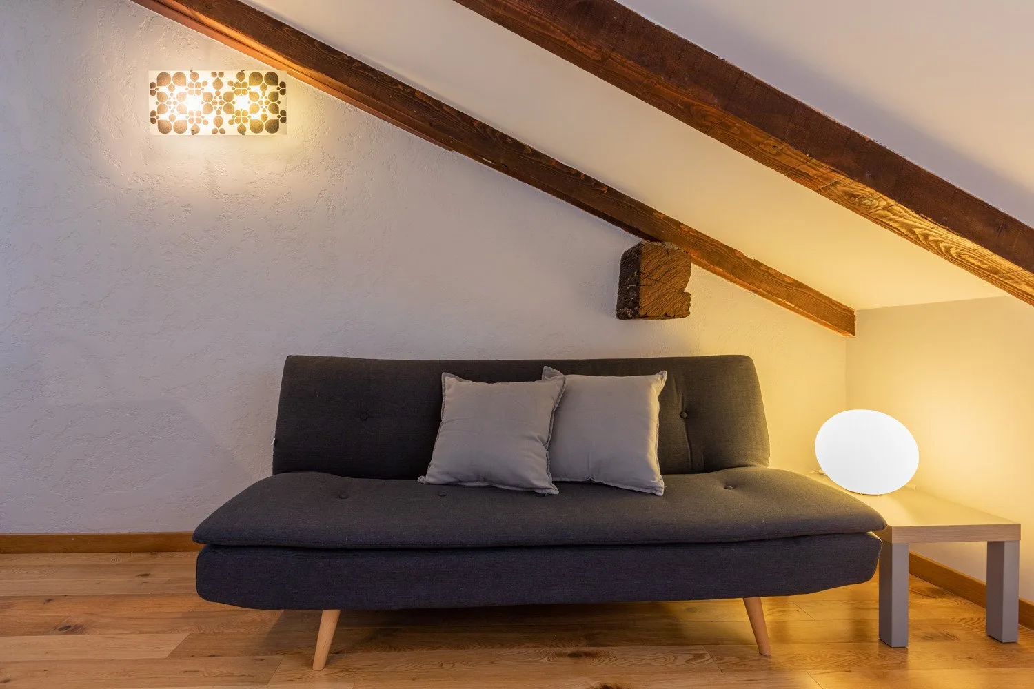 A dark sofa sits beneath exposed wooden beams in a softly lit room.