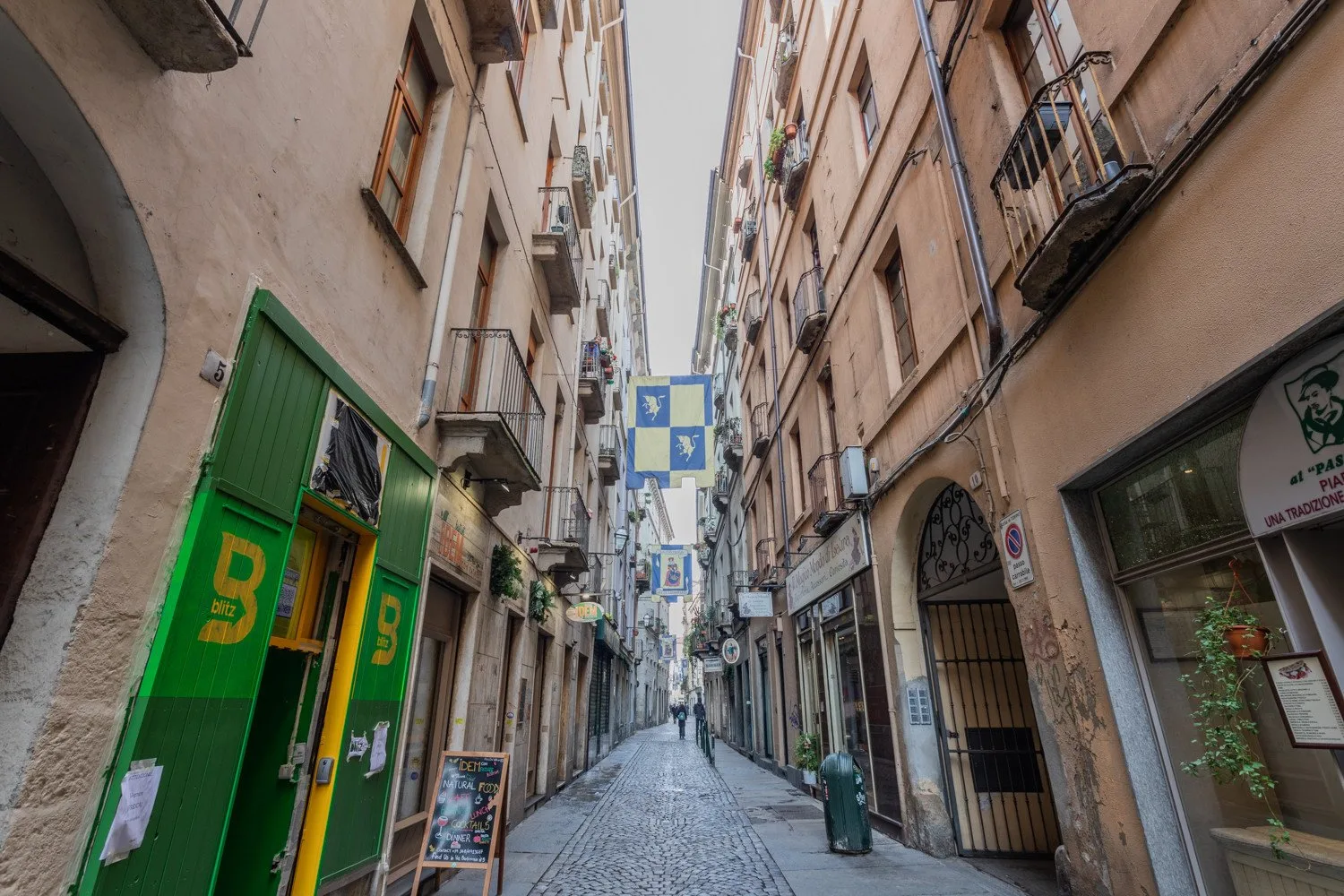A narrow cobbled street runs between tall buildings with shops at street level.