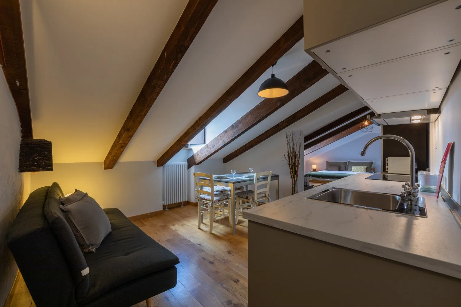 An open-plan kitchen and dining area with a sofa and exposed ceiling beams.