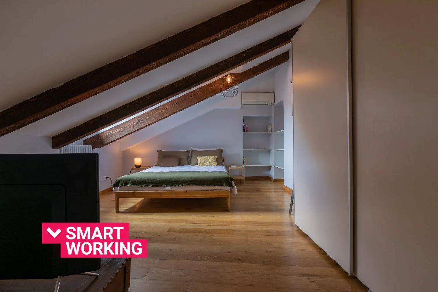 A bedroom with a bed beneath a sloped ceiling and exposed beams.
