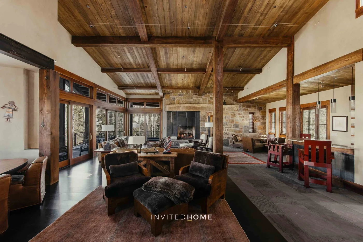A spacious living room with seating around a central table and a stone fireplace.