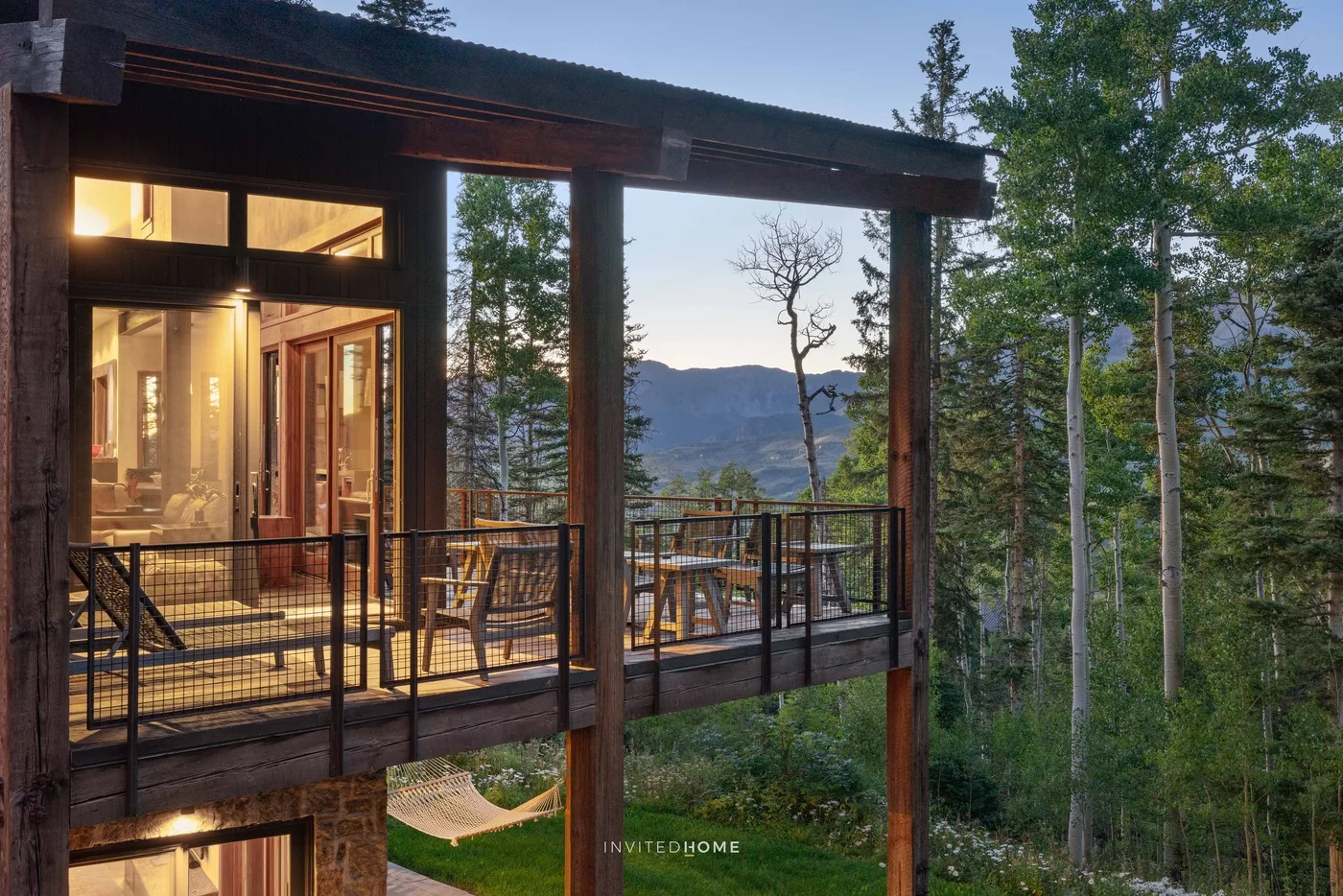 A modern cabin balcony overlooks a forested mountain landscape.