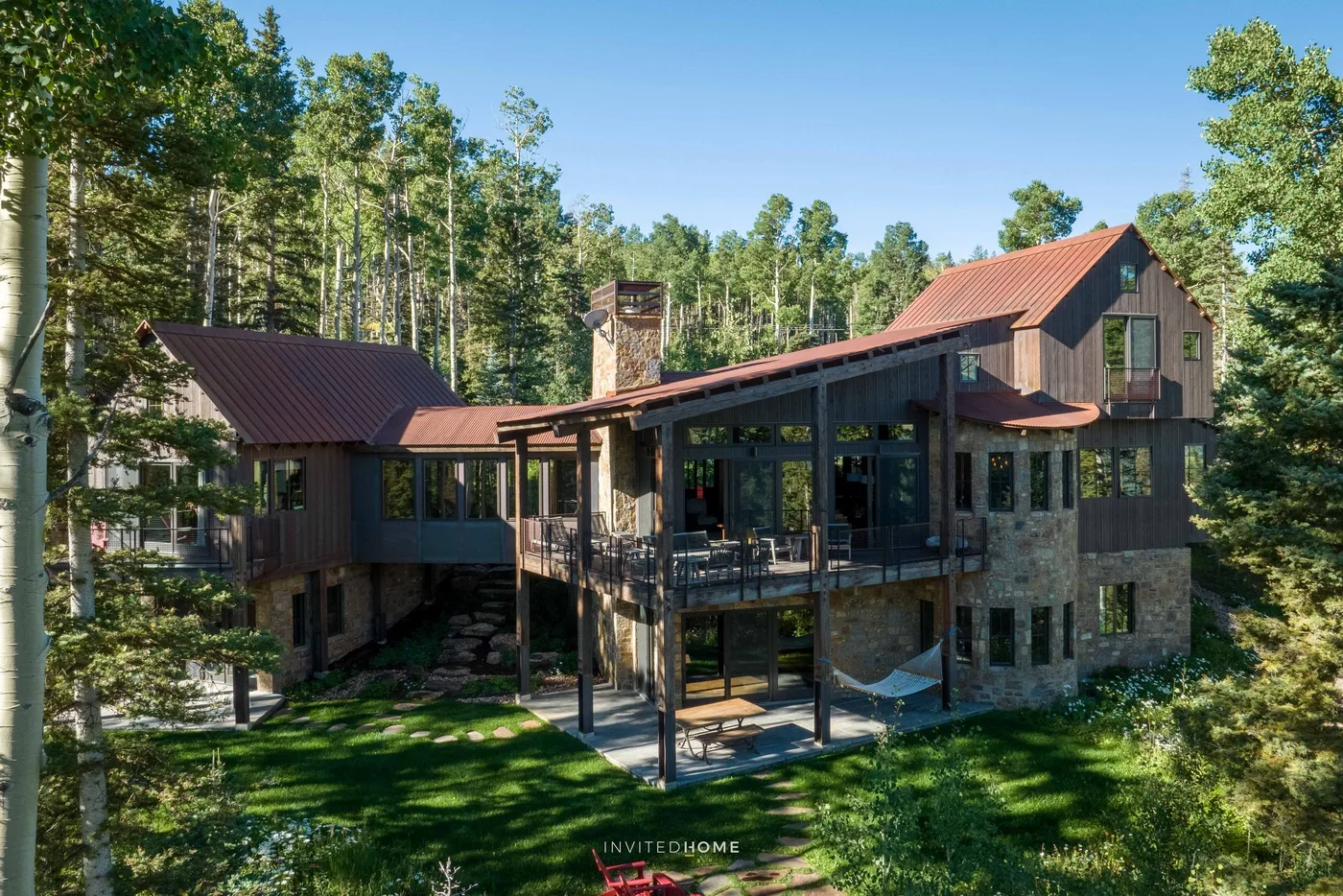 A large house surrounded by trees, with a covered deck overlooking the lawn.