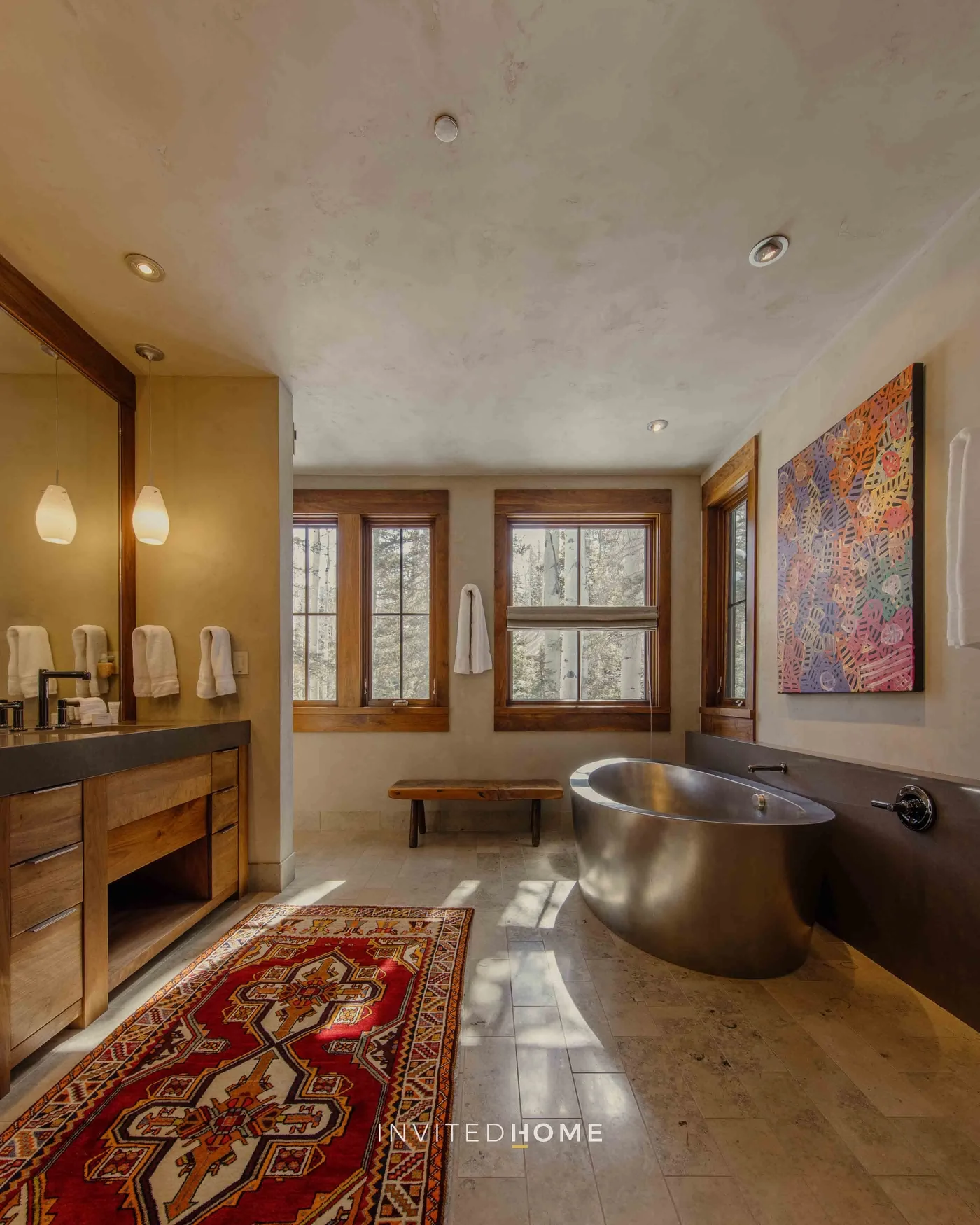 A bathroom with a freestanding bathtub, vanity, windows, and a patterned rug.
