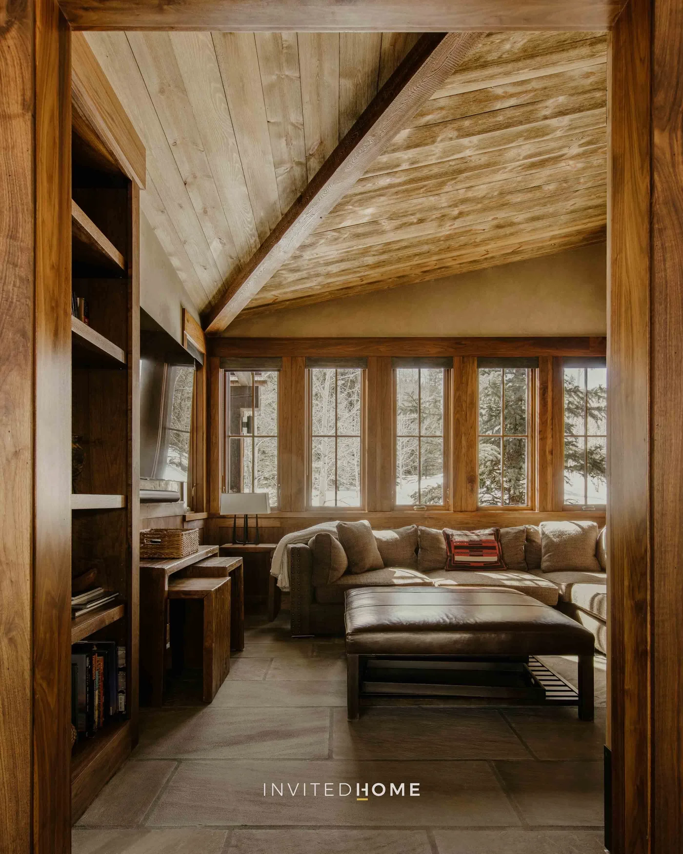 A wood-paneled living room with seating beneath a sloped ceiling and tall windows.